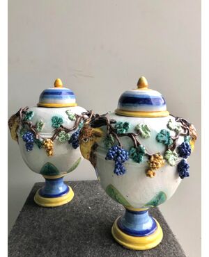 Pair of majolica vases with lids.Decorated with embossed grape shoots and leaf motif.Side sockets with masks.Rubbiani manufacture, Sassuolo.     