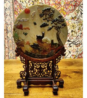 Disco in giada  arricchito con decorazioni di varie pietre all’interno. Provenienza Cina, epoca XX secolo.  Il supporto è in legno patinato ( diametro 30 cm ).