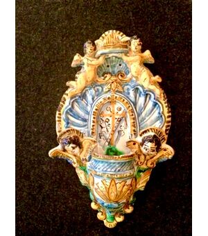 Holy water stoup in majolica with shell motifs, angels, cherubs and cross in the center. Manufacture of Vietri, Campania.     