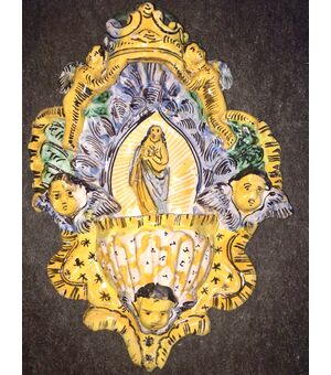Holy water stoup in ribbed majolica with shell-shaped cup and series of angels and figure of Saint in relief in the center. Manufacture of Cerreto Sannita.     