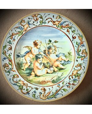 Majolica plate with Raphaelesque and grotesque decoration on the brim and three cherubs in the cavetto.Manifattura Molaroni.Pesaro     