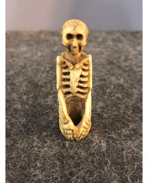 Piccola scultura raffigurante scheletro inginocchiato in osso.