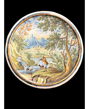 Tondino in maiolica raffigurante cacciatore che spara a selvaggina su sfondo agreste e architetture.Castelli d’Abruzzo.