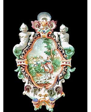 Two-light majolica candlestick wall lamp with grotesque figures on the sides and a central historiated medallion. Battaglia manufacture. Naples.