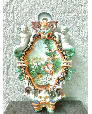 Two-burner majolica applique candlestick with mask, grotesque figures on the sides and central medallion decorated with characters on a rural background.Battaglia Manufacture.Naples     