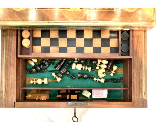 Tavolino da gioco in noce con intarsi. Il piano e’scorrevole e ribaltabile e presenta all'interno scacchiera con scacchi e dama e backgammon.Provenienza:Francia.