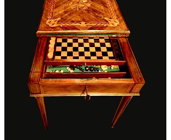 Tavolino da gioco in noce con intarsi. Il piano e’scorrevole e ribaltabile e presenta all'interno scacchiera con scacchi e dama e backgammon.Provenienza:Francia.