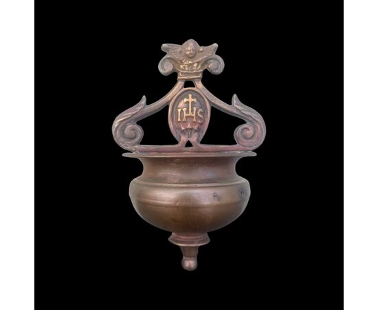 Acquasantiera in bronzo con vaschetta a bordo estroflesso,prese a ricciolo,putto e simbolo berardiniano.