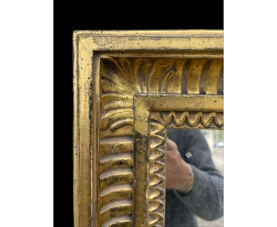 Grande specchiera in legno intagliato con motivi geometrici e vegetali stilizzati e foglia oro.