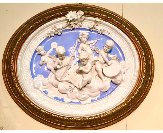 Grande ovale in maiolica con gruppo di angeli musicanti in rilievo in stile robbiano.Manifattura di Angelo Minghetti.Bologna.