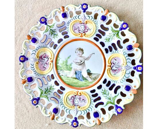 Perforated plate in majolica with rocaille motifs in relief, decoration with putto in the cavetto and grotesque and vegetable motifs on the brim.Ginori manufacture.     