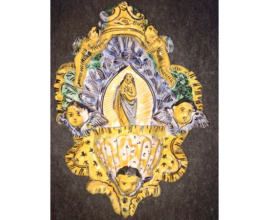 Holy water stoup in ribbed majolica with shell-shaped cup and series of angels and figure of Saint in relief in the center. Manufacture of Cerreto Sannita.     