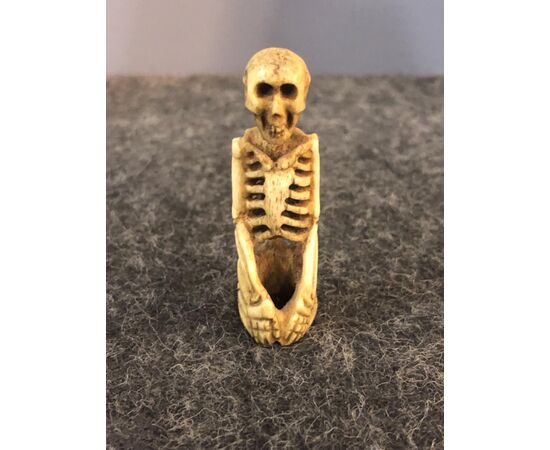 Small sculpture depicting a skeleton kneeling in bone.     