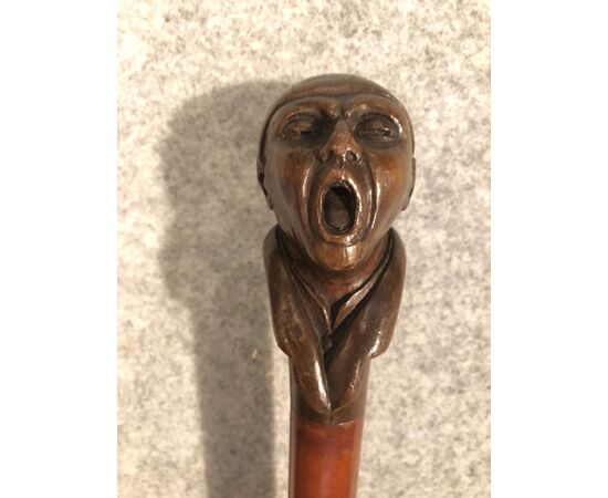 Stick with wooden knob depicting screaming male figure.     