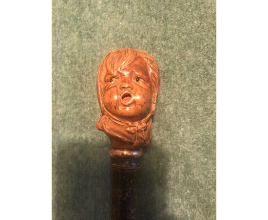 Bastone con pomolo in legno raffigurante testa di bambino che piange.
