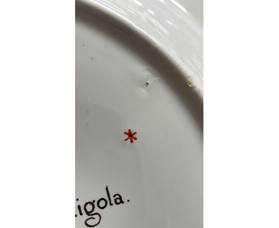 Piatto in porcellana con tondo centrale raffigurante scena paesaggistica. Iscrizione sul retro.Manifattura Ginori Doccia.
