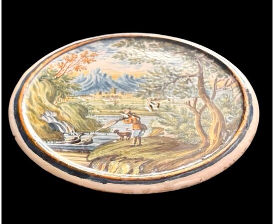 Tondino in maiolica raffigurante cacciatore che spara a selvaggina su sfondo agreste e architetture.Castelli d’Abruzzo.