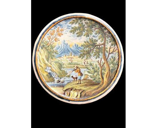 Tondino in maiolica raffigurante cacciatore che spara a selvaggina su sfondo agreste e architetture.Castelli d’Abruzzo.