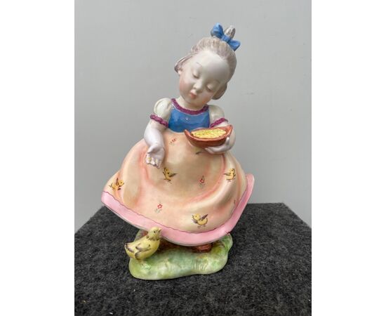 Polychrome earthenware figure depicting a girl feeding a chick. Signed     