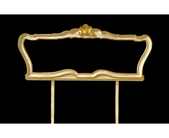 Testiera letto in legno scolpito con motivi rocaille color crema e oro.