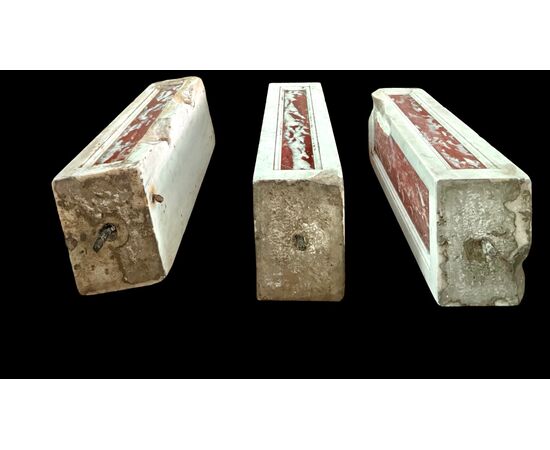 Three architectural elements in marble with a white frame and a variegated red central section.