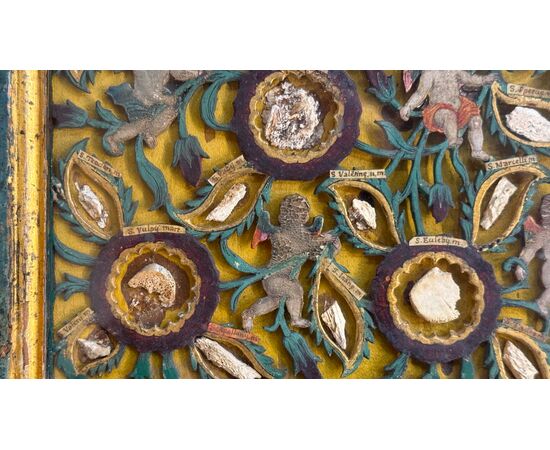 Quadro reliquiario con composizione in legno traforato in rilievo con putti e motivi vegetali.
