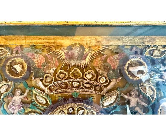 Quadro reliquiario con composizione in legno traforato in rilievo con putti e motivi vegetali.