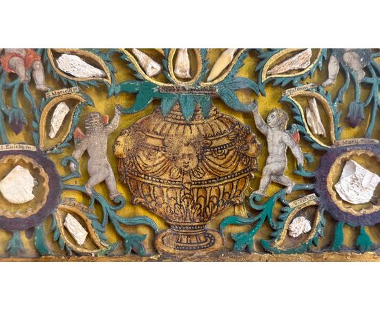 Reliquary painting with openwork wood composition in relief with putti and vegetal motifs. Reliquary painting with openwork wood composition in relief with putti and vegetal motifs.
