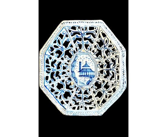 Octagonal raised plate in pierced majolica with geometric motifs and architectural scene in the center. Savona.