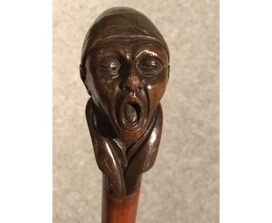 Bastone con pomolo in legno raffigurante figura maschile urlante.