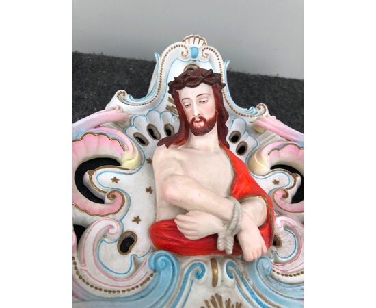 Acquasantiera in porcellana bisquit traforata con motivi rocaille e con figura a mezzo busto di Cristo legato.