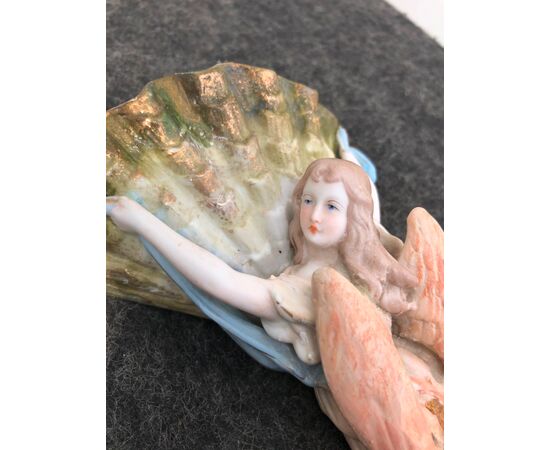 Acquasantiera in porcellana bisquit raffigurante angelo di spalle che regge la coppa a conchiglia.Italia.