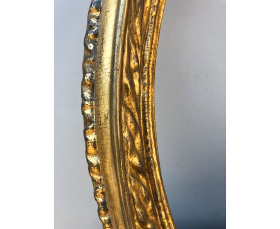 Cornice ovale in legno intagliato con motivo a foglie e foglia oro.