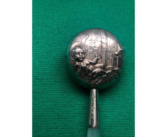 Baby rattle in silver with scene of Baby Jesus and protector Angel. Mother of pearl handle.     