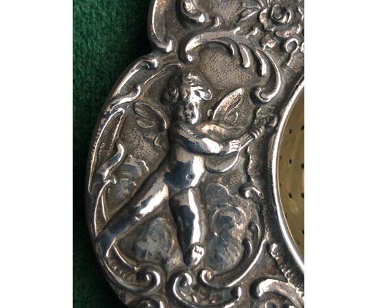 Silver tea strainer with 4 cherubs, birds, floral and rocaille motifs.     