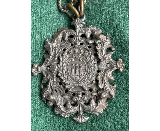 Medaglia in metallo argentato e traforato con motivi vegetali rocaille e tre torri simbolo di San Marino.