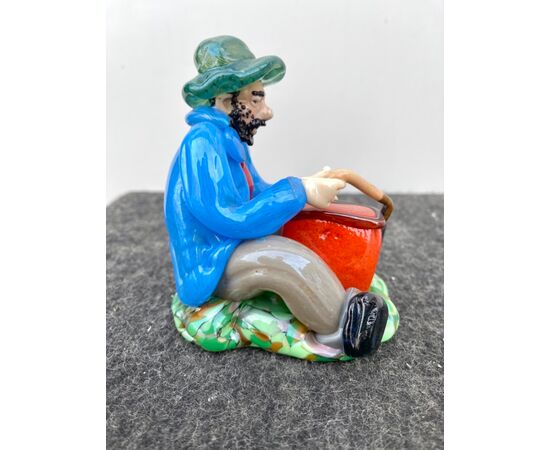 Glass sculpture depicting a seated character with basket, Bohemia.     