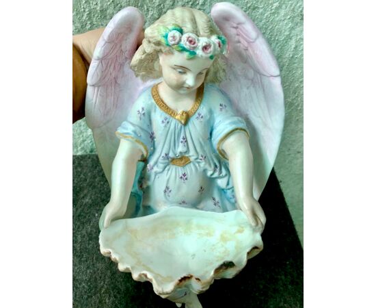 Acquasantiera  in porcellana bisquit raffigurante angelo con corona di fiori che regge la coppa a forma di conchiglia.Francia.