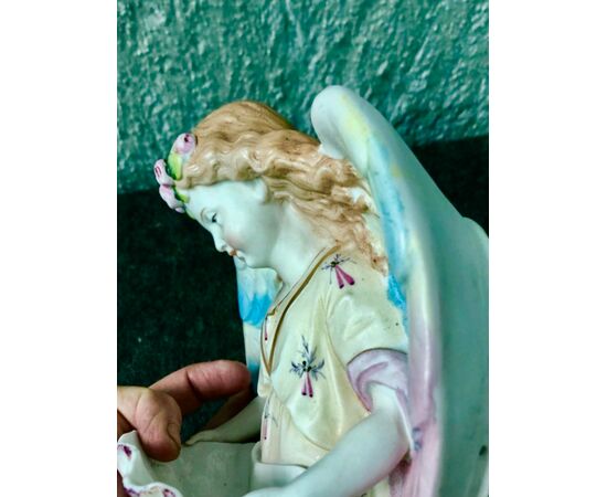Acquasantiera in porcellana bisquit raffigurante angelo con corona di fiori che regge la coppa a forma di conchiglia.Francia.