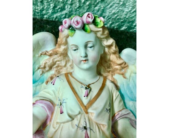Acquasantiera in porcellana bisquit raffigurante angelo con corona di fiori che regge la coppa a forma di conchiglia.Francia.