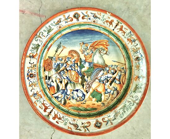 Majolica plate decorated with battle scene in the cavetto and Raphaelesque motifs on the brim. Manufacture of Oreste Ruggeri, Pesaro.     