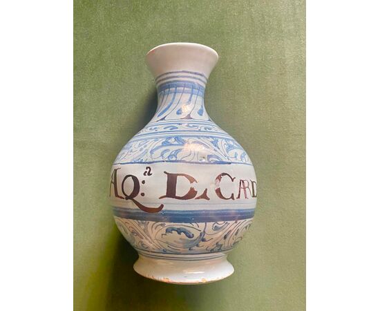 Bottiglia in maiolica a sfondo berettino con decoro a motivi vegetali e geometrici stilizzati e cartiglio epigrafe.Faenza.