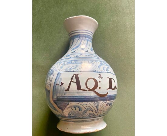 Bottiglia in maiolica a sfondo berettino con decoro a motivi vegetali e geometrici stilizzati e cartiglio epigrafe.Faenza.