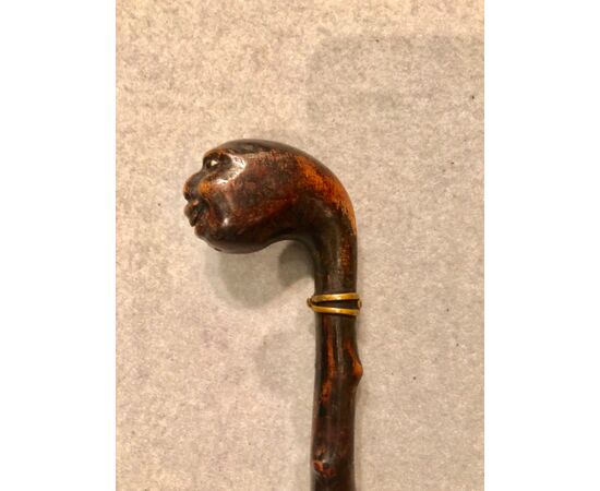 Stick in a single piece made of ebonized fruit wood with a knob representing a grotesque head.     