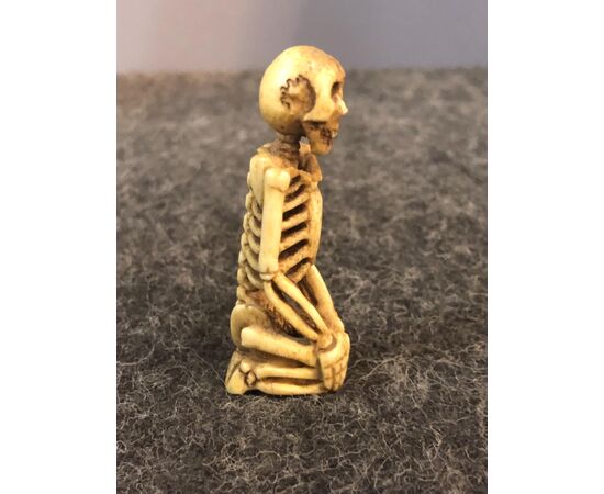Piccola scultura raffigurante scheletro inginocchiato in osso.