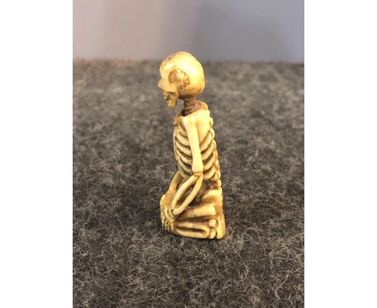 Small sculpture depicting a skeleton kneeling in bone.     