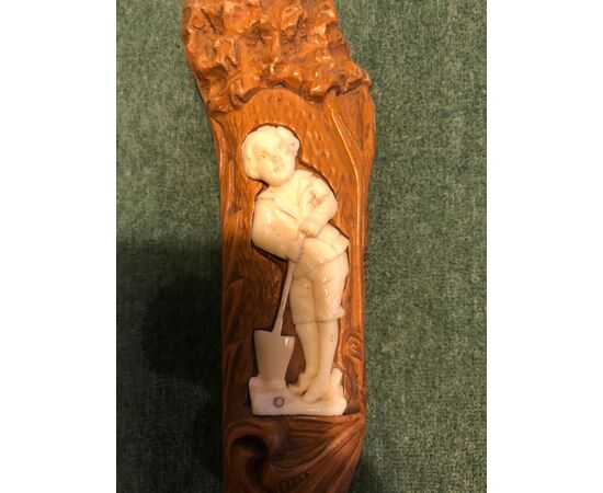 Bastone con pomolo in legno con bassorilievo  raffigurante figura maschile con vanga. 