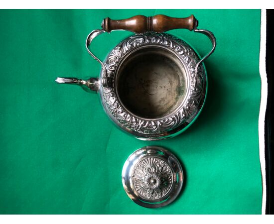 Silver-plated copper teapot with stylized plant motifs and wooden handle.     