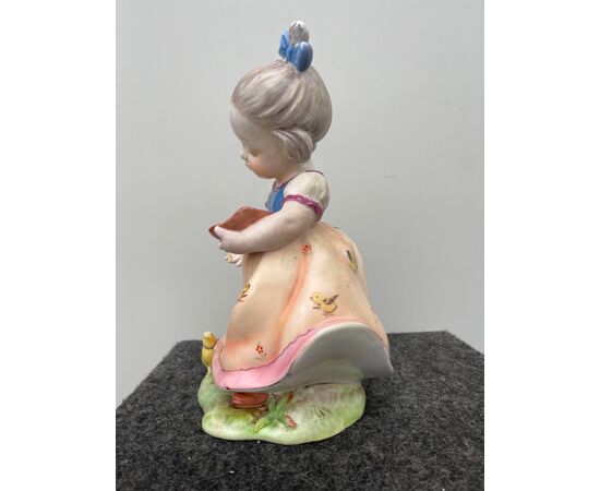 Polychrome earthenware figure depicting a girl feeding a chick. Signed     