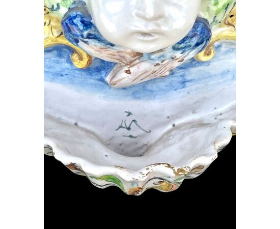 Acquasantiera in maiolica con cherubino e vasca a conchiglia.Decoro a motivi vegetali stilizzati.Manifattura di Angelo Minghetti.Bologna.